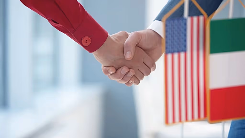 İki kişinin tokalaşması, arka planda ABD ve İtalya bayrakları