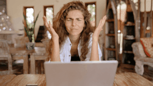 Bir kadın, bilgisayar karşısında ellerini iki yana açarak hayal kırıklığı yaşıyor; uzaktan çalışmanın getirdiği zorlukları simgeliyor.